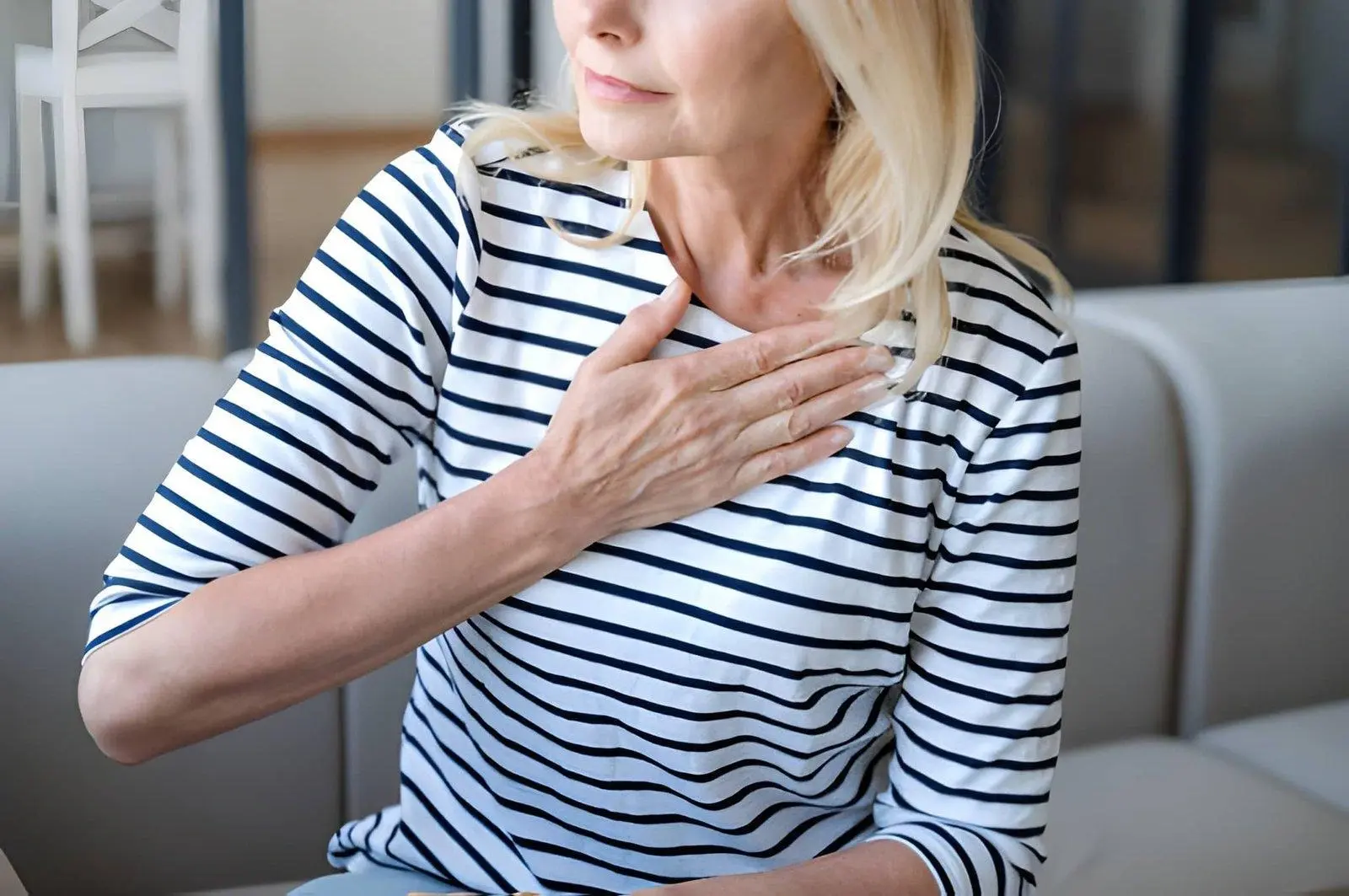 Woman in a striped shirt sitting on a sofa with her hand resting on her upper chest.