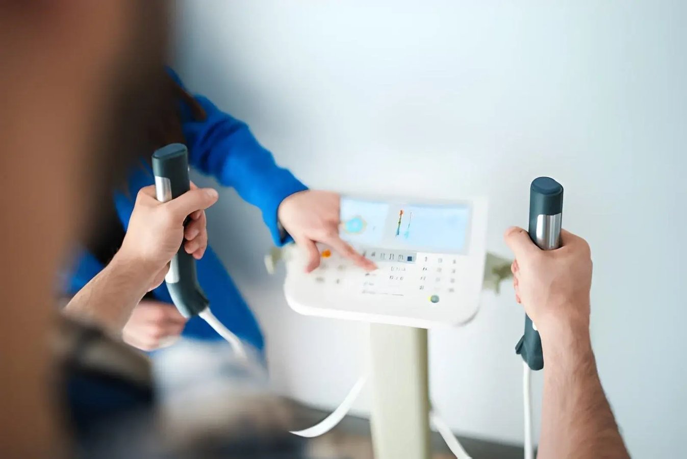 Person holding body composition scanner handles while a healthcare professional points to the display.