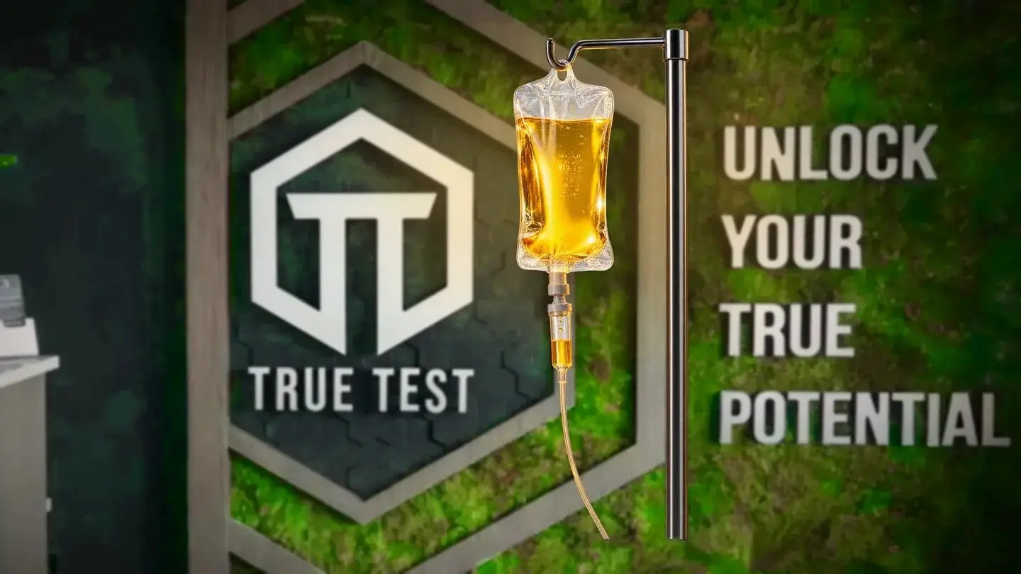 A vitamin IV drip in front of the True Test moss logo wall