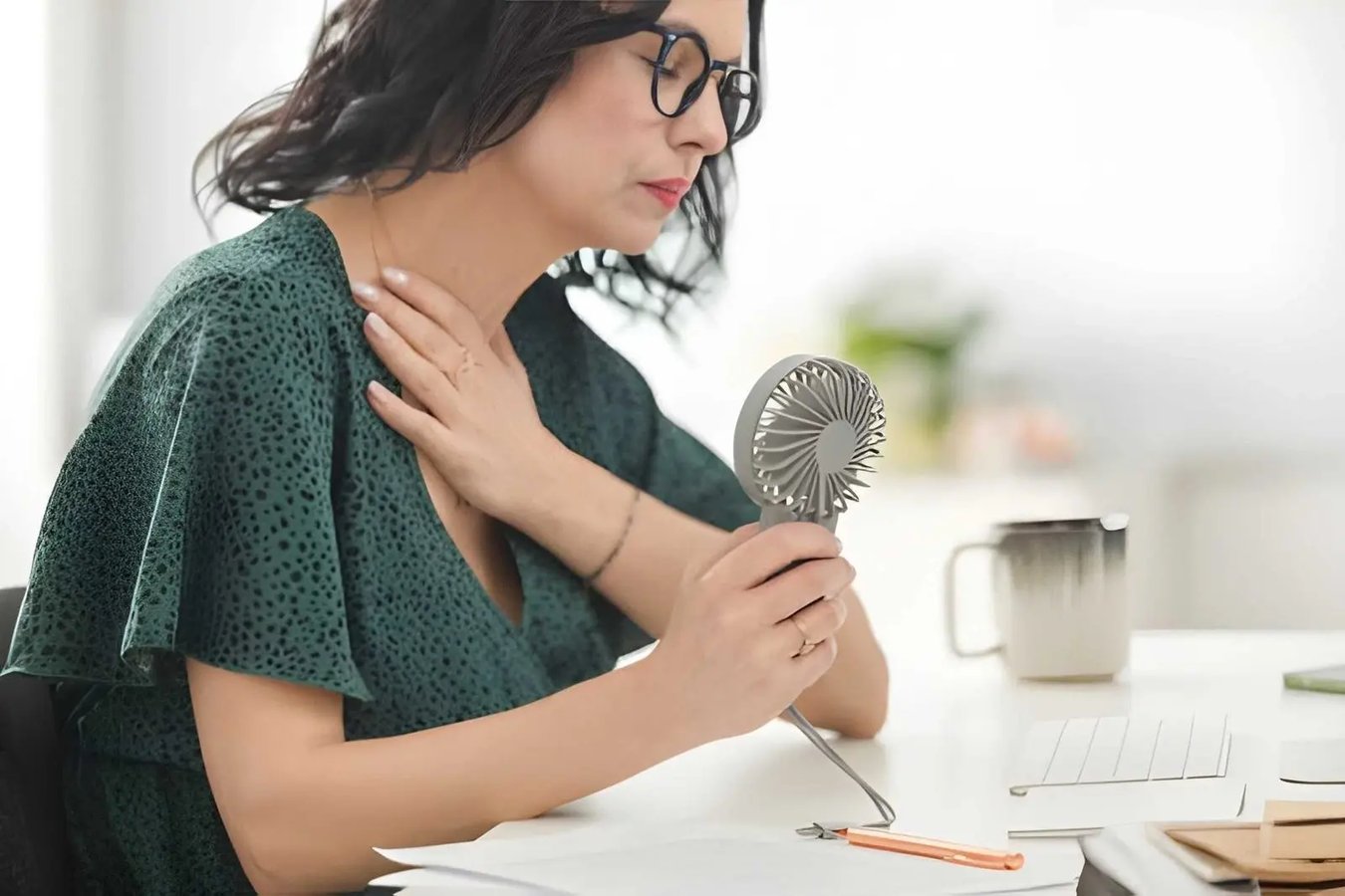 Woman experiencing a hot flash while using a handheld fan at home