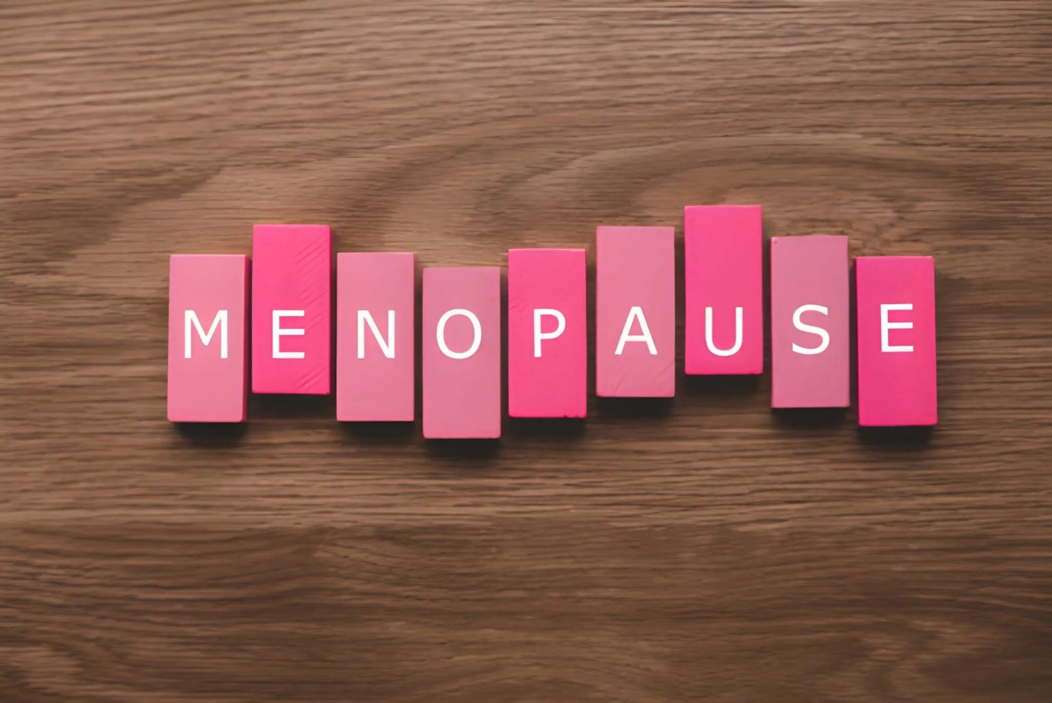 Pink blocks spelling menopause on a wooden surface for a perimenopause vs menopause article.